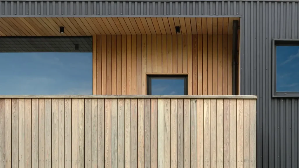 Façade de maison moderne avec un balcon en bois et des planches verticales en contraste avec le revêtement métallique sombre