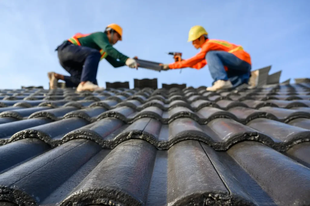 Sélectionnez l'accent sur les tuiles de toit Arrière-plan flou d'un couvreur travaillant sur le toit d'une maison Utilisez une perceuse pour percer les vis pour fixer les tuiles de ciment