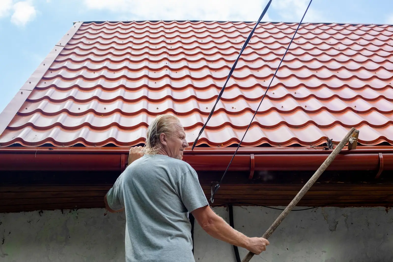 Un homme mûr nettoie la gouttière d'un tuyau d'évacuation sur le toit de sa maison des feuilles d'automne et des débris